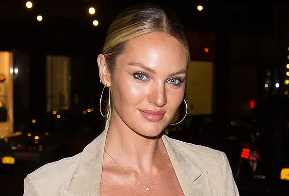 A person with blonde hair and hoop earrings smiles at night, wearing a light-colored outfit.