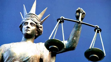 Statue of Lady Justice holding scales against a clear blue sky.