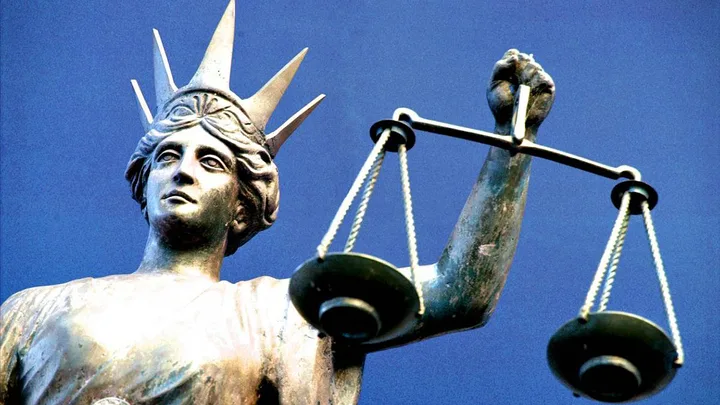 Statue of Lady Justice holding scales against a clear blue sky.