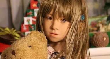 A realistic humanoid figure with long hair, holding a teddy bear, in a decorated room with presents and ornaments.