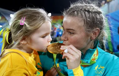 An athlete and a young girl kiss an Olympic gold medal, both wearing Australian team colors.