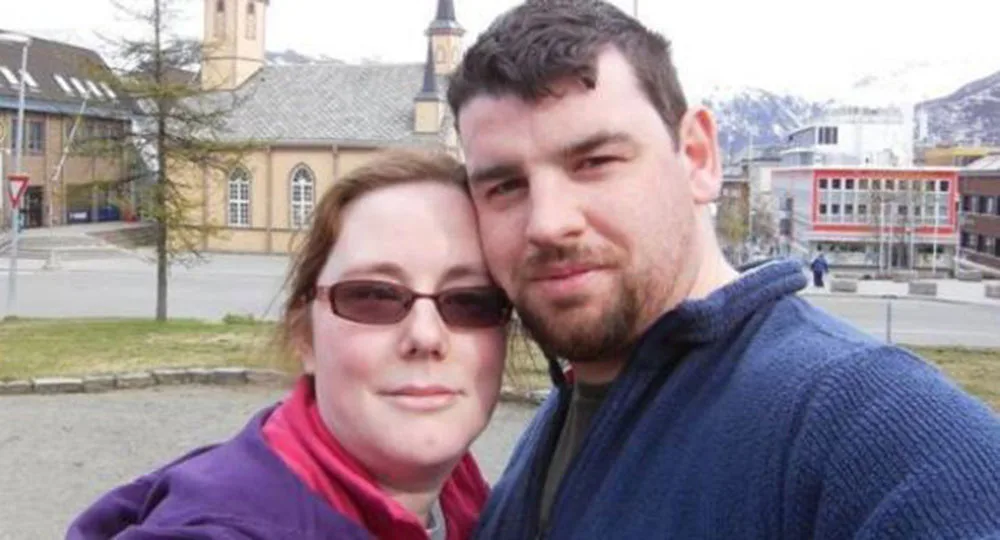Couple posing for a selfie outdoors with a church and mountains in the background.