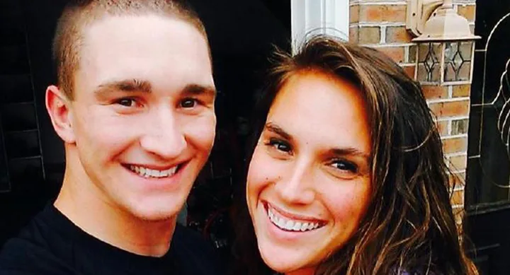 Two people smiling warmly in front of a brick wall and door.