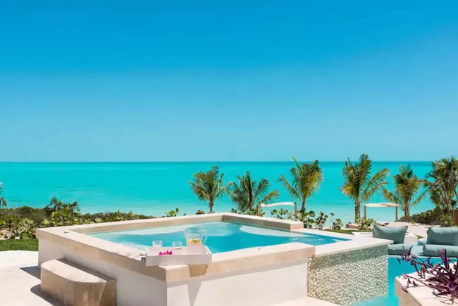 Luxurious hot tub overlooking a tropical ocean with clear blue skies and palm trees in the background.