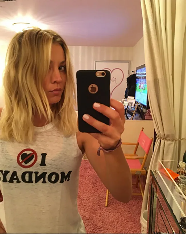 A woman with blonde hair takes a mirror selfie wearing a shirt that says "I [no symbol] Mondays."
