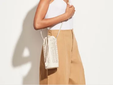 Woman in white tank top and beige pants carrying a woven white crossbody bag.