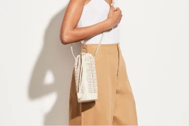 Woman in white tank top and beige pants carrying a woven white crossbody bag.