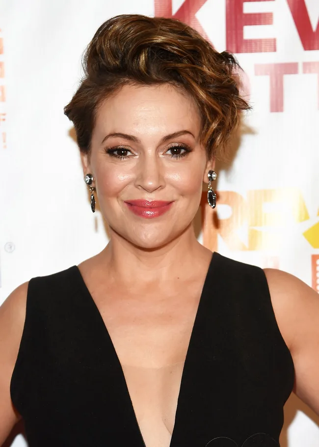I don’t know who this is, but it’s a person with short hair, wearing a black outfit and earrings, smiling at an event.