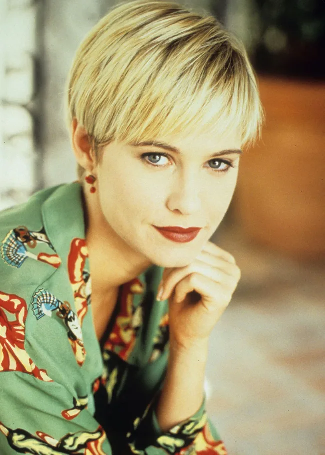 A woman with short blonde hair wearing a colorful robe, gazing thoughtfully at the camera.