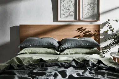 A neatly made bed with green and gray linens, a wooden headboard, and two abstract line art frames on the wall above.