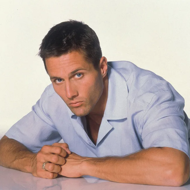 Man in a light blue shirt, looking ahead with hands clasped.
