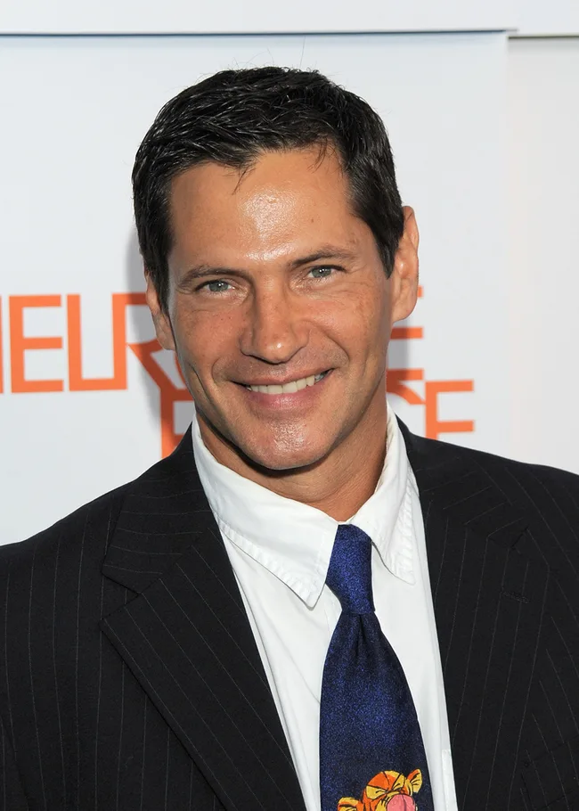 A man in a suit and tie, smiling at an event with a backdrop featuring text.
