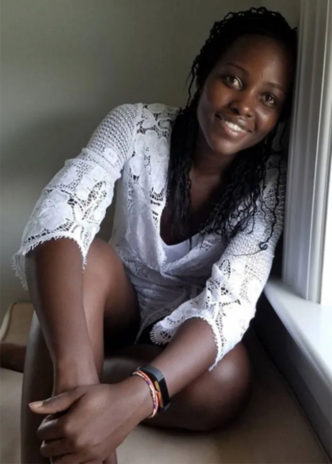Smiling woman in white lace outfit sitting by a window with natural light.
