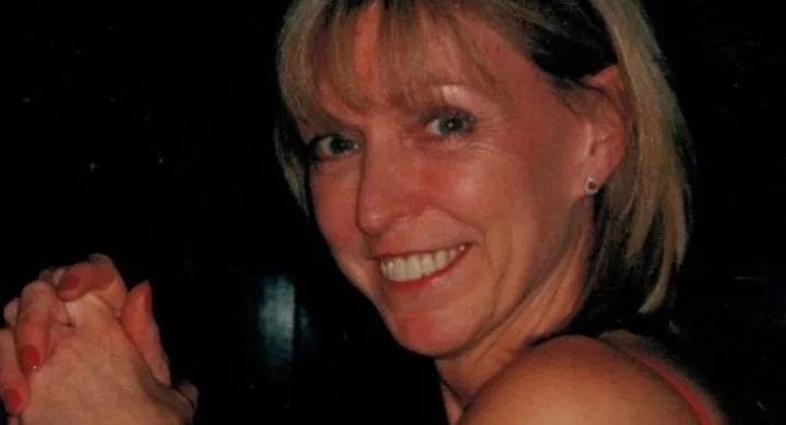 A woman with blonde hair smiling warmly, clasping her hands.