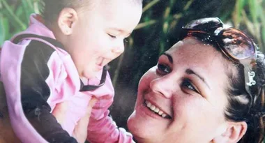 A smiling woman holds a laughing baby dressed in pink and black, creating a joyful moment together.