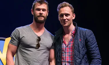 Two men standing together at an event, one in a grey t-shirt and the other in a plaid shirt with a quilted jacket.
