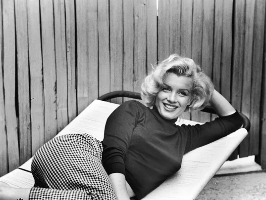 Person reclining on a lounger, smiling, in a fenced outdoor setting.