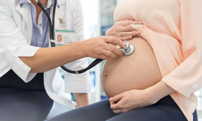 Doctor using a stethoscope to examine a pregnant woman's belly during a medical check-up.