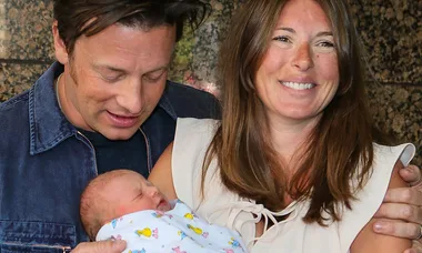 A couple smiling at their newborn baby wrapped in a colorful blanket.