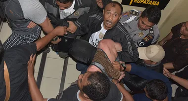 A group of people surround a man being carried by several individuals inside a building hallway.