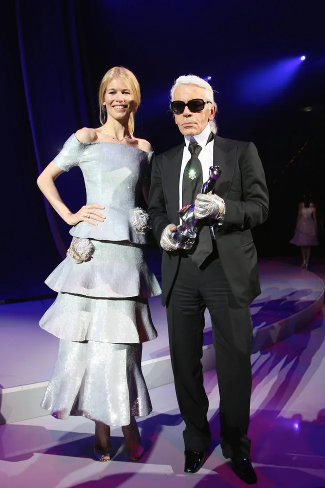 Two individuals in formal attire on stage; one holds a trophy.