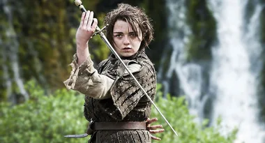 A person in medieval clothing holds a sword poised to strike, with a waterfall in the background.