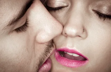 A close-up of a couple kissing, showing the man's stubble and the woman's pink lipstick and nose piercing.