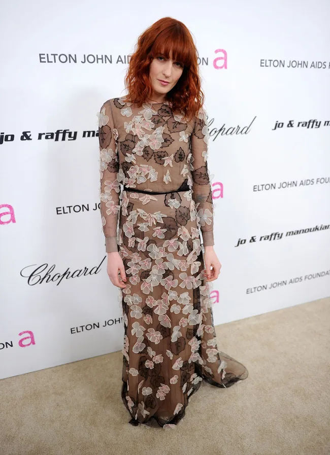 Red-haired woman in a floral sheer gown at an Elton John AIDS Foundation event.
