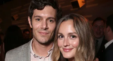 Two individuals smiling at a social event, with blurred background and warm lighting.