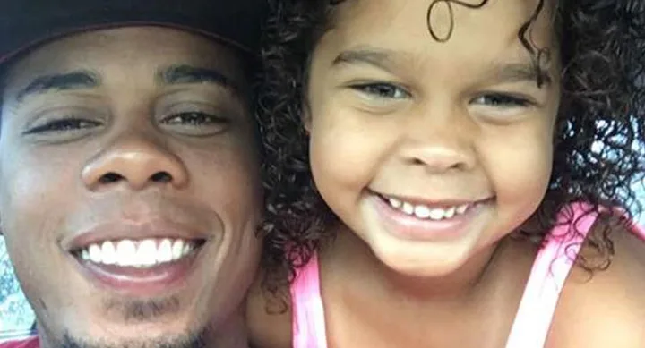 Man in a cap smiling with a young girl, both having curly hair and bright smiles, close-up selfie.