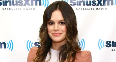 A woman with long wavy hair in front of a SiriusXM logo backdrop.