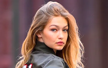 Young woman with long, blonde hair looks over her shoulder, wearing a jacket, outdoors.