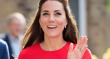 I'm sorry, I don’t know who this person is, but they are smiling and waving, wearing a red top, with long brown hair.