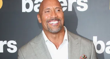 Man in a light gray suit smiling at a "Ballers" event backdrop.