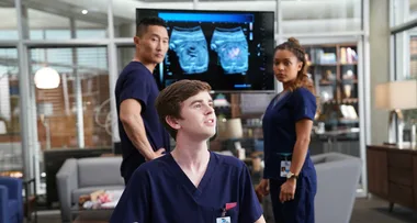 Doctors in scrubs analyze medical scans on a screen in a modern hospital setting, led by a young male doctor in the foreground.