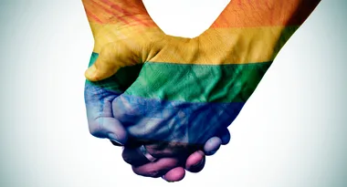 Two hands clasped together with a rainbow flag overlay, symbolizing support for LGBTQ+ rights.