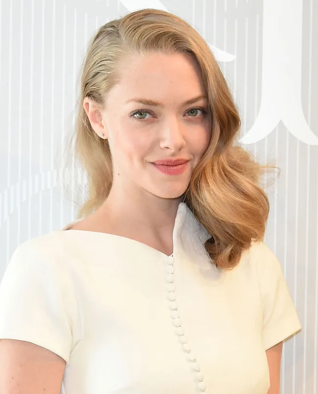 A person with long blonde hair wearing a white buttoned top, smiling at the camera.
