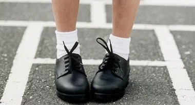 Child wearing black lace-up shoes and white socks on striped pavement.