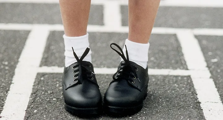 Child wearing black lace-up shoes and white socks on striped pavement.