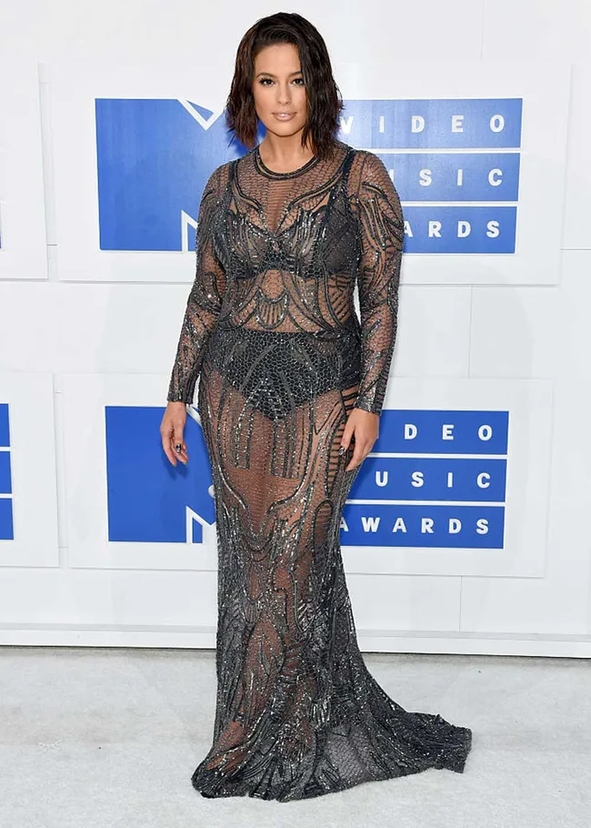A woman in a sheer, beaded gown poses on the red carpet at a Video Music Awards event.