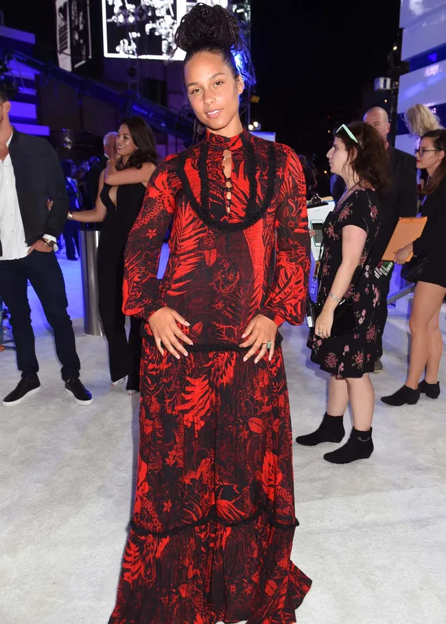 Woman in a red and black patterned dress poses at an event, surrounded by people and blue lighting in the background.