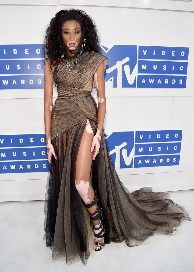 Model in a stylish asymmetrical gown at the MTV Video Music Awards, standing in front of the event's logo backdrop.