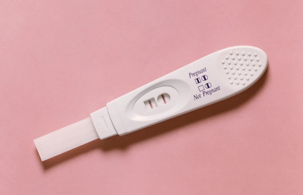 Positive pregnancy test with two visible lines, placed on a pink background.