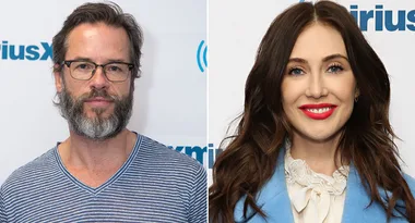 Male with glasses and beard in striped shirt; female with long hair in blue blazer, red lipstick smiling at event.