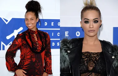 Two women at a red carpet event; one in a patterned red dress, the other in a black lacy outfit with a jacket.