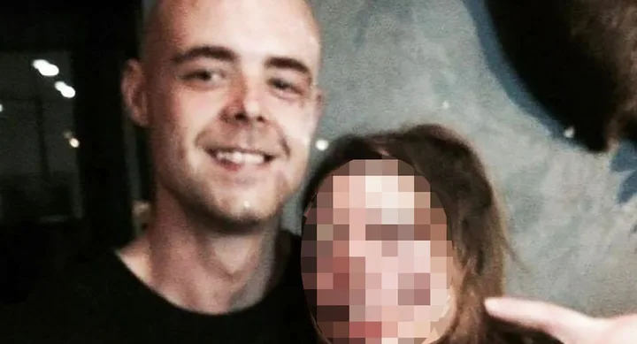 A man with a shaved head smiles at the camera; another person's face is pixelated next to him.