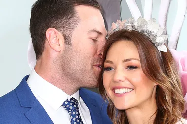Man in blue suit whispers to smiling woman wearing a decorative headpiece.