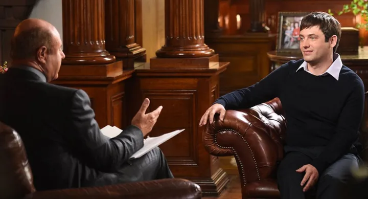 Two people sitting in leather chairs having a conversation in a warmly lit room with wooden decor and framed photos.
