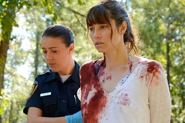 A police officer arrests a woman with a blood-stained shirt in a forest scene from "The Sinner."