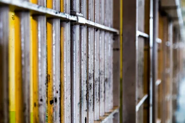Close-up of a row of rusty prison cell bars with a yellow background, suggesting confinement or incarceration.